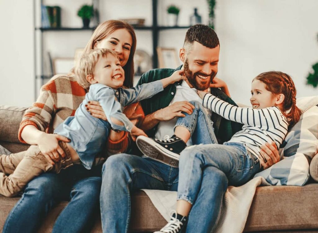 Austin TX Family Insurance - The Lambert Agency A happy family with two children laughing together on a sofa, illustrating the peace of mind provided by life and health insurance from The Lambert Agency in Austin, TX.