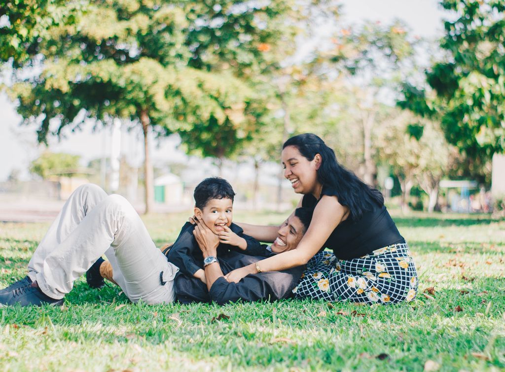 Photo by Patricio Ledeill Happy family enjoying a playful moment lying on grass in a sunny park.