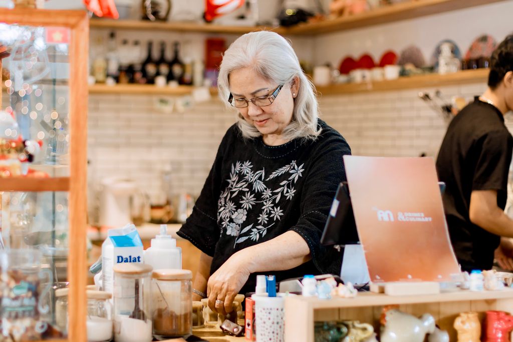 Photo by 🇻🇳🇻🇳Nguyễn Tiến Thịnh 🇻🇳🇻🇳 Senior woman working behind the counter in a cozy, warmly lit coffee shop.
