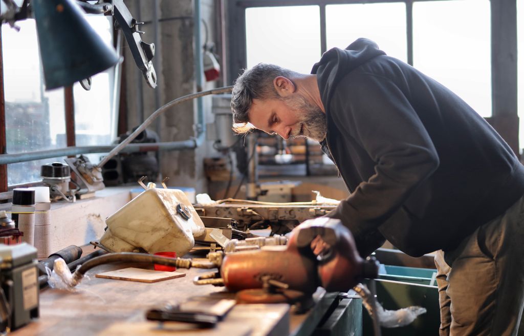 Photo by Andrea Piacquadio Side view of brutal male worker in casual wear standing at workbench and fixing metal details while using tools and working in workshop